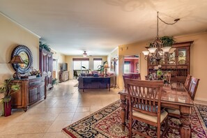 A spacious living room with a large dining table, a chandelier, and a view of the kitchen.