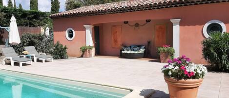 Un espace aménagé au bord de la piscine, avec des chaises longues, un petit coin salon doté de coussins et des plantes en pot.