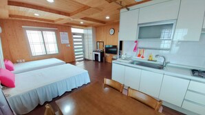 A room with two beds, a wooden dining table, a kitchen with a sink, and a TV.