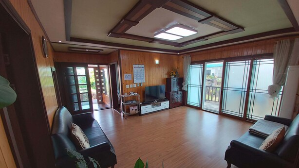 A spacious living room with wooden flooring, a sofa set, a TV, and a sliding glass door leading to a balcony.