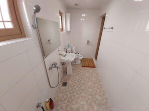 A small, clean bathroom with white tiles, a sink, toilet, and a shower. - Feeling Good House (Jeju City)