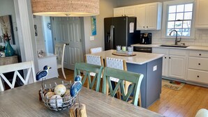 Una cocina moderna con armarios blancos, una isla central y un comedor con mesa y sillas.
