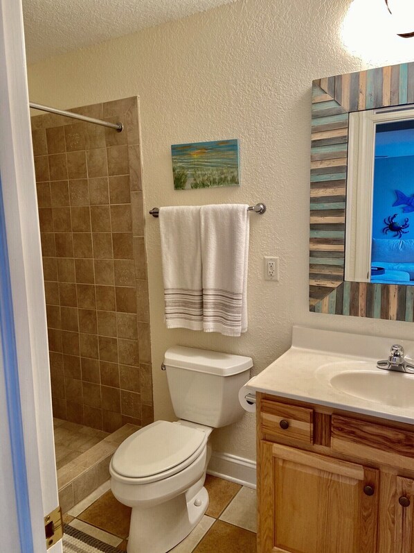 A bathroom with a toilet, shower, sink, and wooden cabinets.