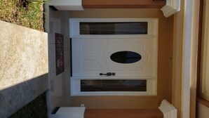 En vit dörr med en glaspanel och ett litet fönster, placerad i en beige vägg med en sockel av betong.