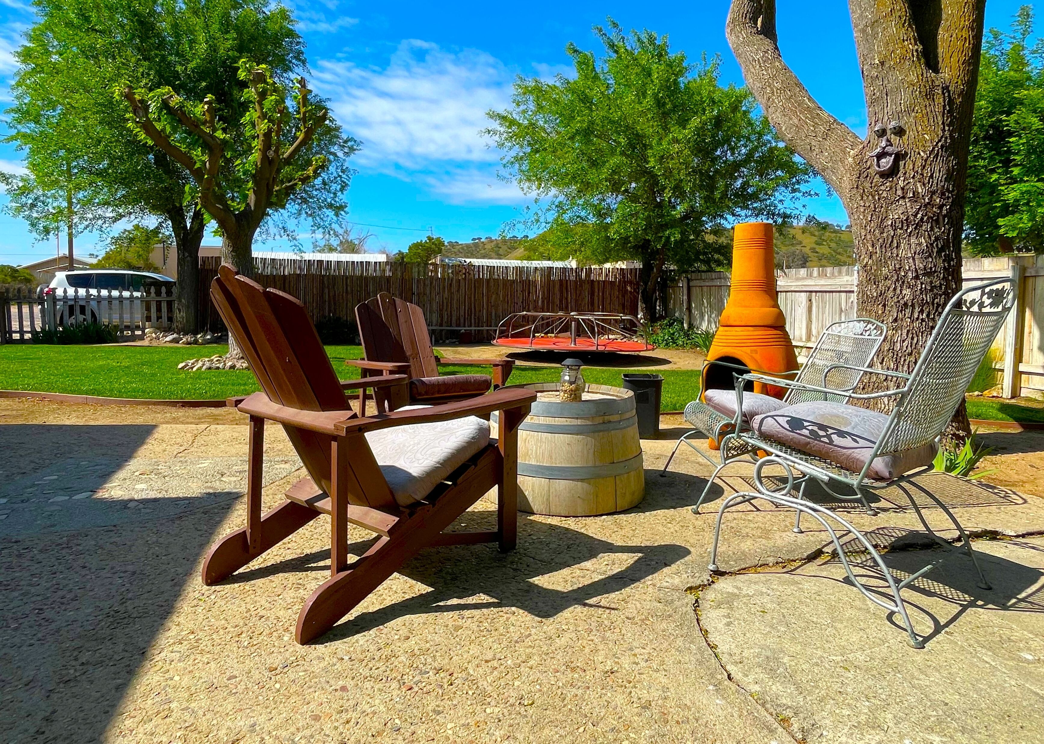 A patio with wooden rocking chairs and a metal chair, a barrel, and a large orange planter.