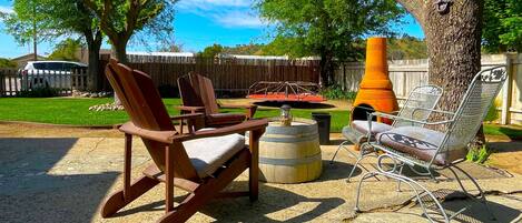 A patio with wooden rocking chairs and a metal chair, a barrel, and a large orange planter.