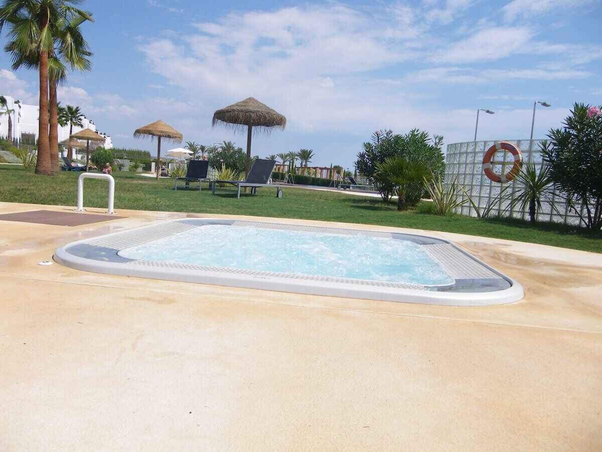 A swimming pool with lounge chairs and umbrellas, surrounded by palm trees and a clear sky.