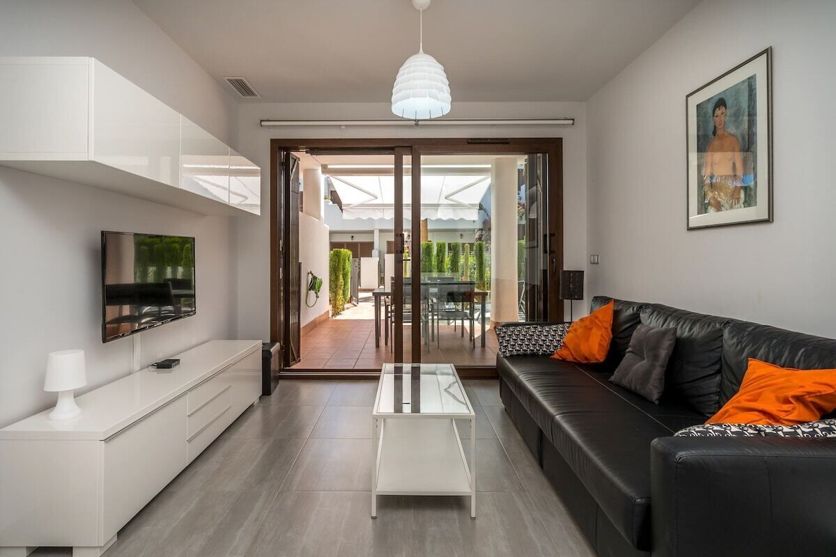A modern living room with a sofa, coffee table, TV, and a glass door leading to an outdoor area.