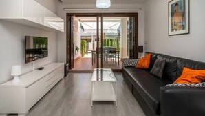 A modern living room with a sofa, coffee table, TV, and a glass door leading to an outdoor area. - Apartamento Rosa (Mar de Pulpi) (San Juan de los Terreros)