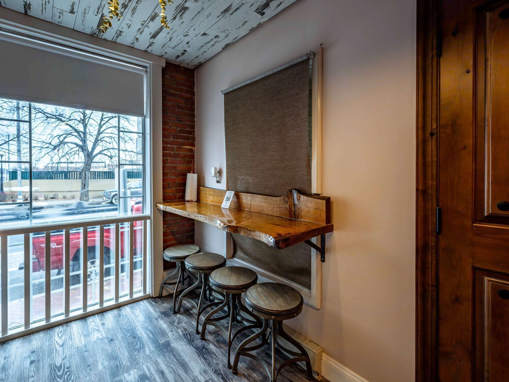 A corner seating area with a wooden bench and stools, a large window, and a view of the outside.