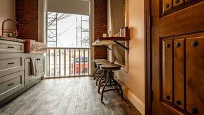 Une cuisine avec un plancher en bois, un mur en briques et une porte blanche donnant sur l’extérieur.