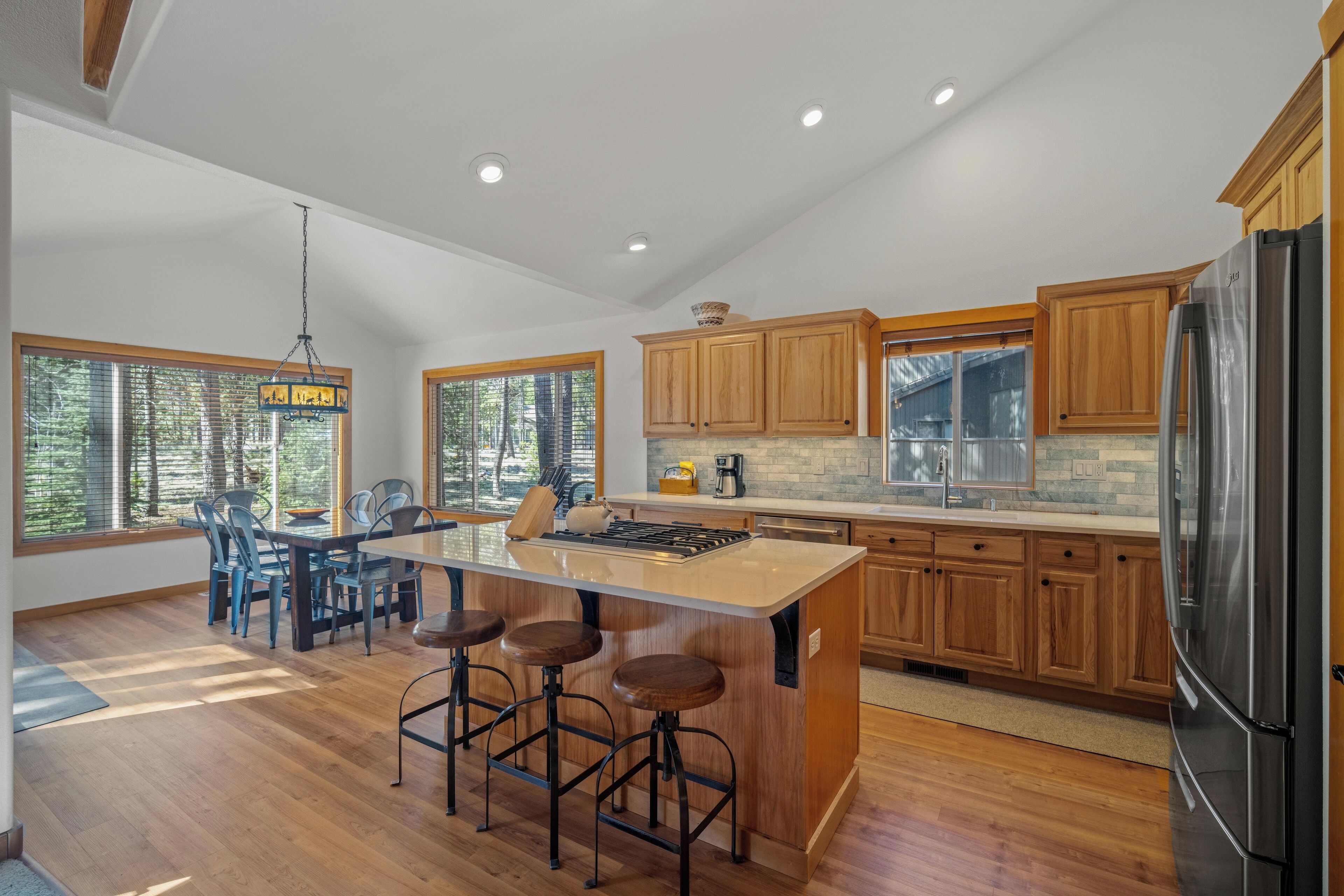 A modern kitchen with wooden cabinets, a stainless steel refrigerator, and a central island with bar stools.