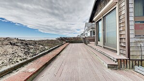 Ein Strandgrundstück mit einem gepflasterten Weg, der zu einem modernen Haus mit großen Fenstern und einem Balkon mit Blick auf den Strand führt.