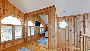 Ein Zimmer mit Holzvertäfelung, großen Bogenfenstern, einer Spiegelwand und einem blau gemusterten Teppich.