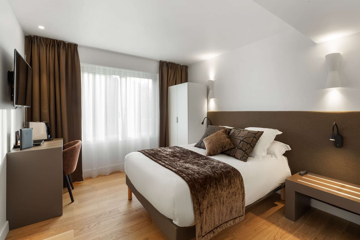 Ein modernes Hotelzimmer mit einem großen Bett, einem Schreibtisch, einem Stuhl und einem Fernseher.