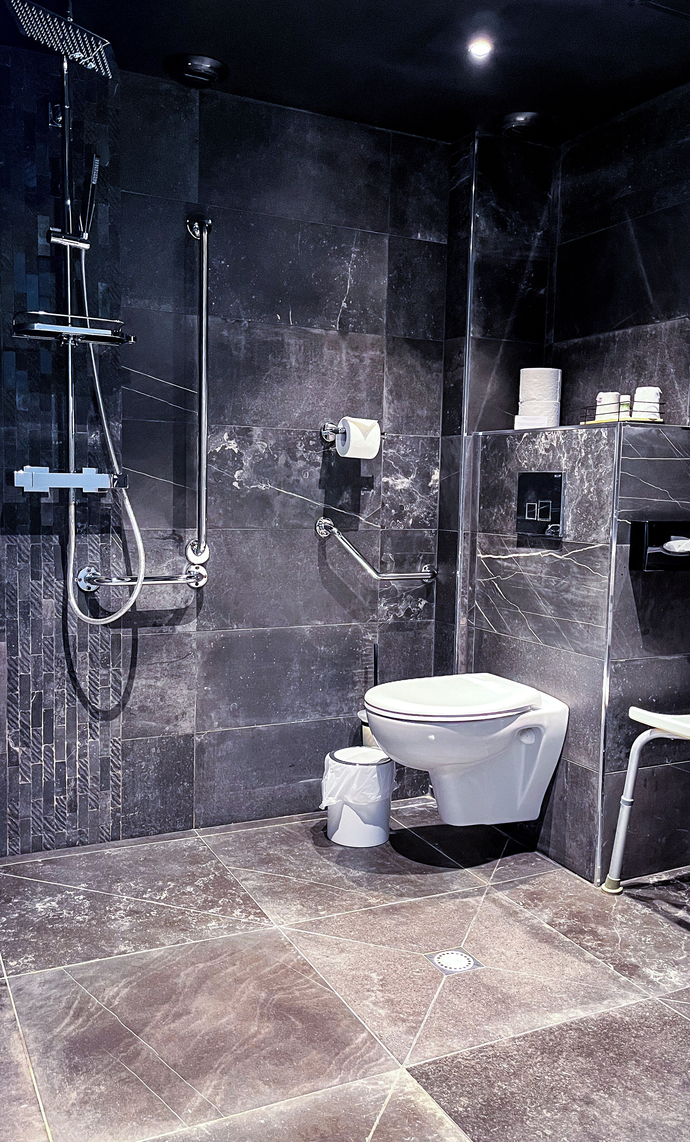 Ein modernes Badezimmer mit einer gläsernen Duschkabine, einer weißen Toilette und einem Boden aus Marmorplatten.