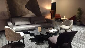 A modern lounge area with a grey sofa, two armchairs, a coffee table, and a potted plant.
