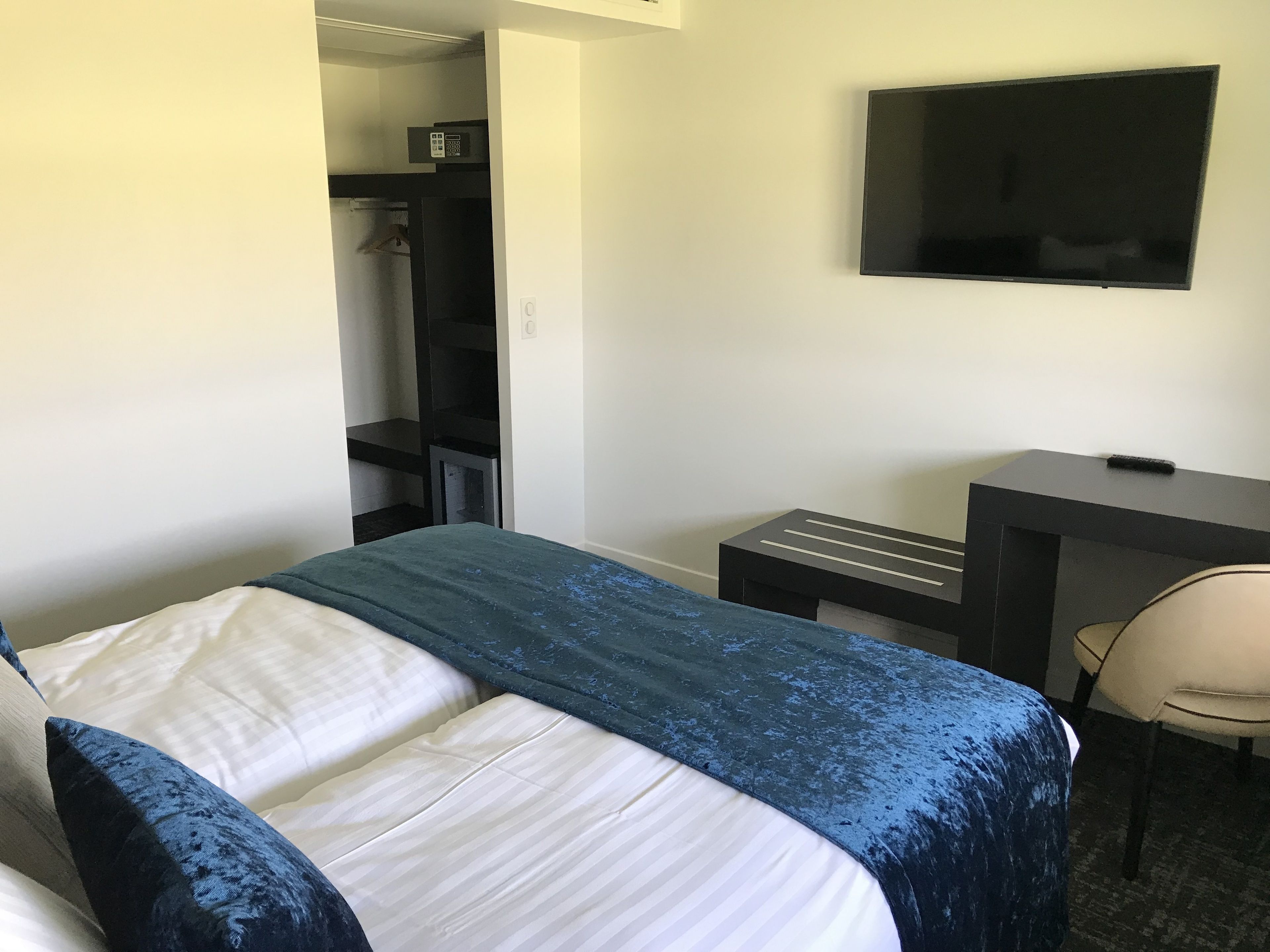 A hotel room with a bed, a desk, a chair, a TV, and a closet.