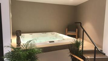 A modern bathroom with a freestanding bathtub, a wooden chair, and potted plants.