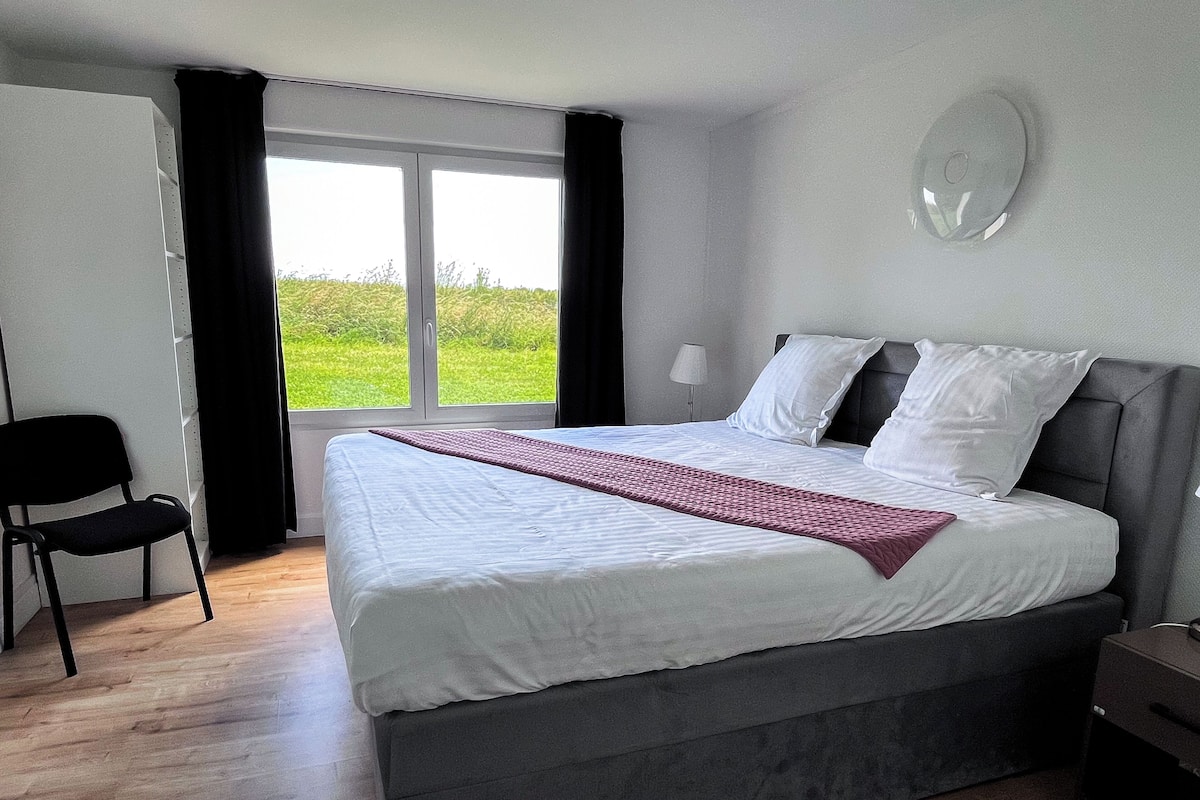 Ein Schlafzimmer mit einem großen Bett, einem Sessel, einem Fenster mit Vorhängen und einer Lampe.