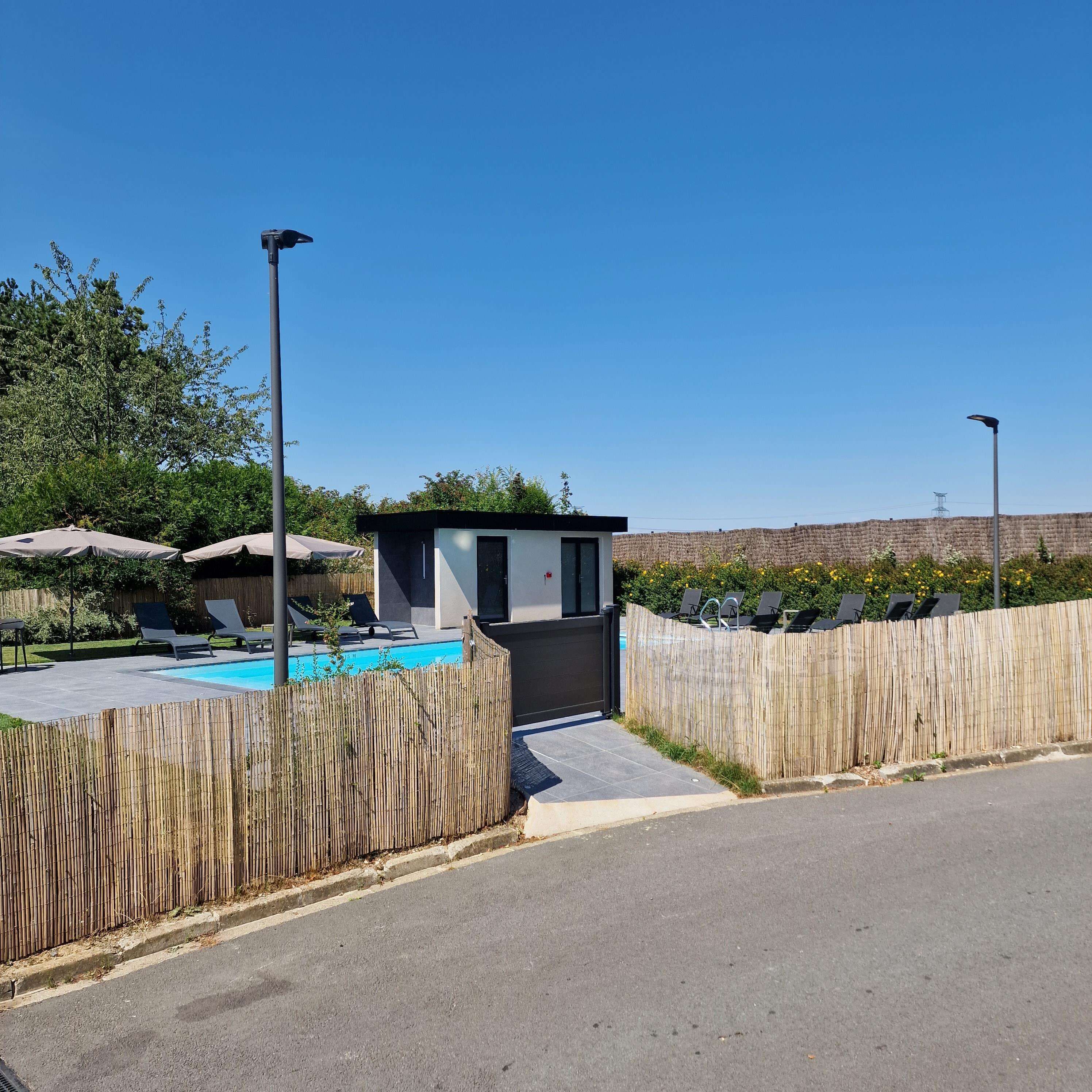 Un espace piscine extérieur moderne, agrémenté d’un petit bâtiment, de chaises longues et d’une clôture en bois.