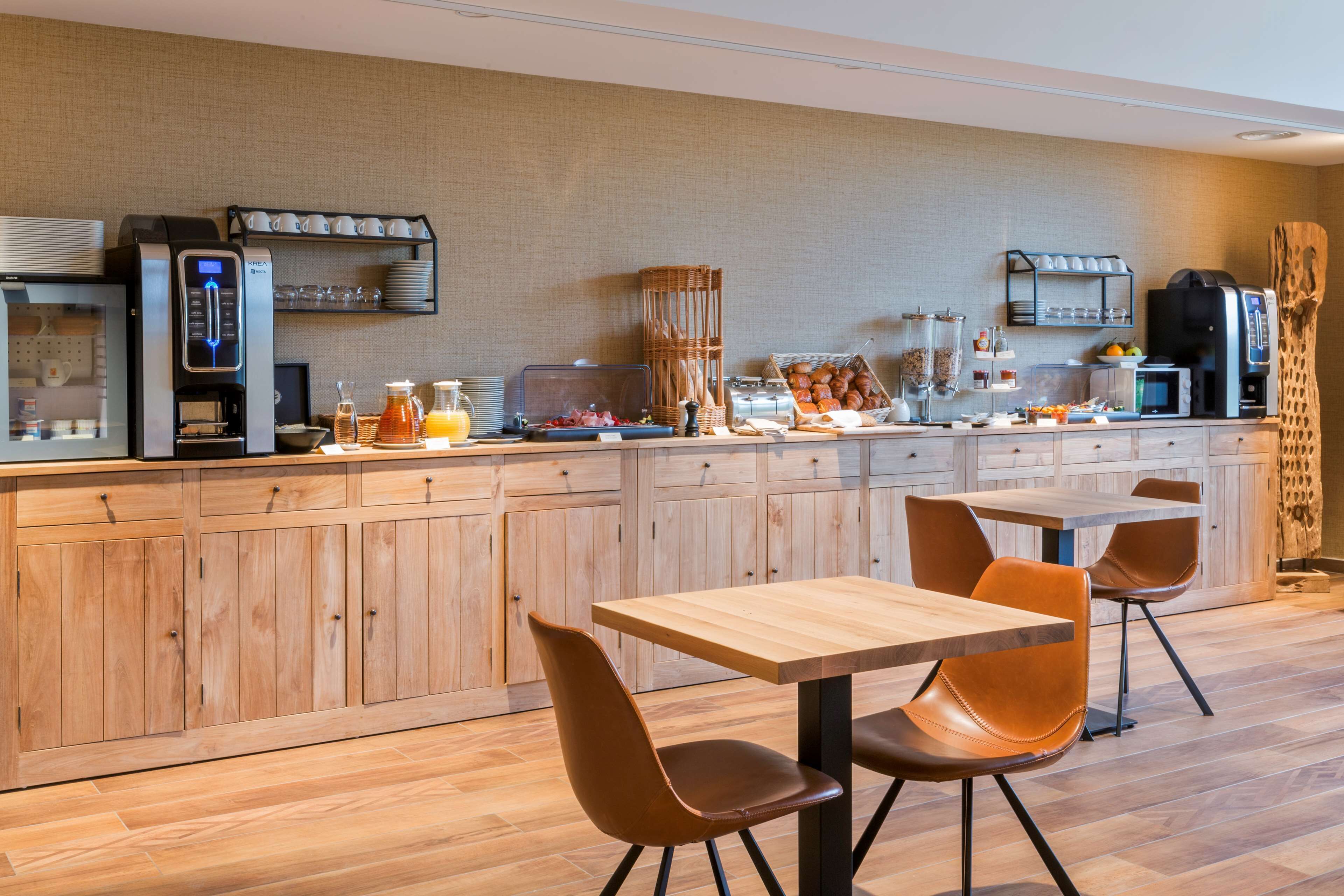 A modern kitchen with a coffee station, wooden cabinets, and a dining area with two tables and chairs.