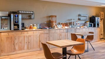 A modern kitchen with a coffee station, wooden cabinets, and a dining area with two tables and chairs.
