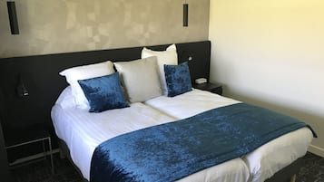A neatly made bed with a white and blue bedspread, a dark headboard, and multiple pillows in shades of white, blue, and grey.