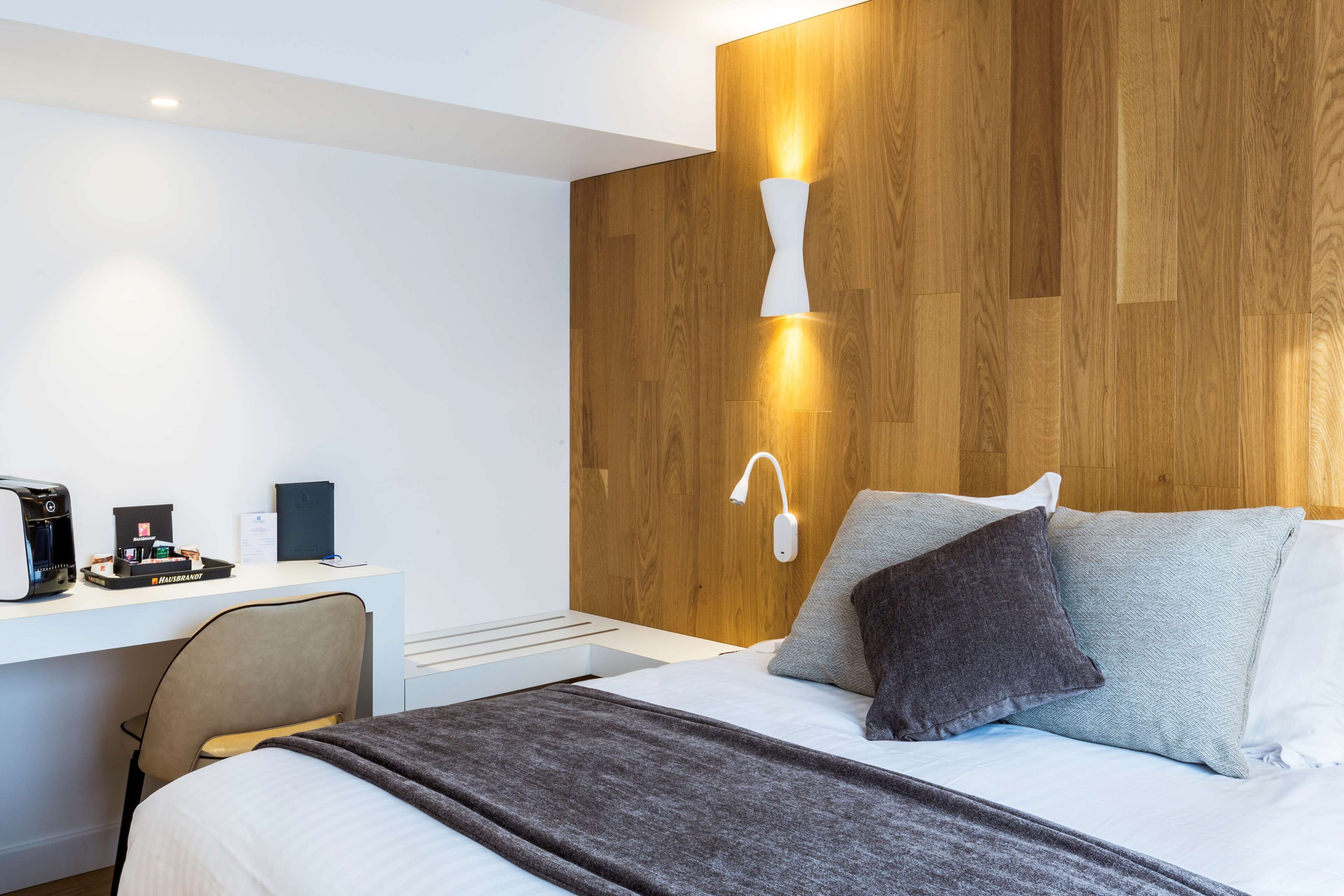 Ein modernes Hotelzimmer mit einer Wand aus Holzpaneelen, einem Schreibtisch mit Kaffeemaschine und einem Bett mit Kissen.