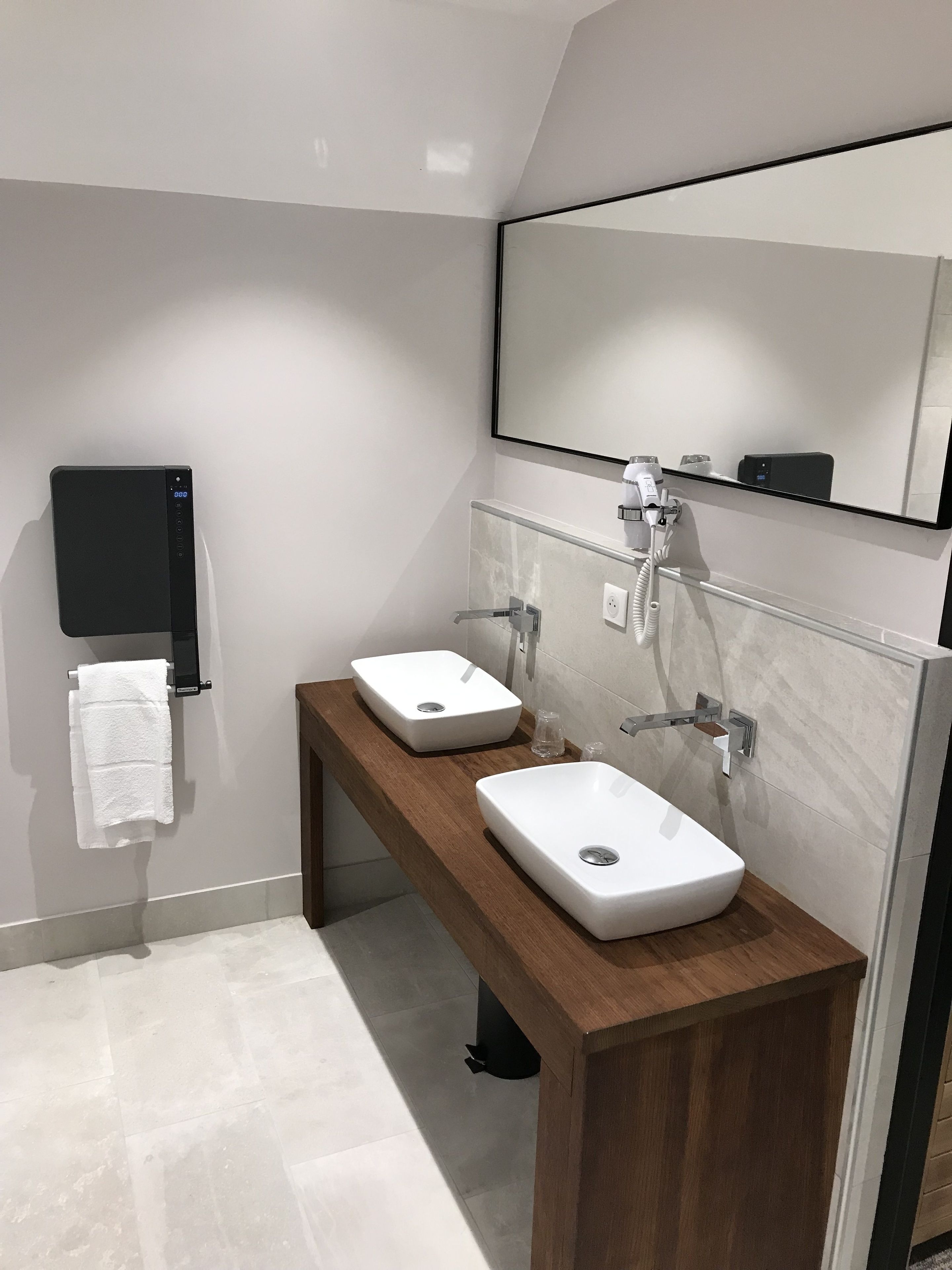 Ein modernes Badezimmer mit zwei Waschbecken, einem Handtuchhalter, einem Spiegel und einem Föhn.