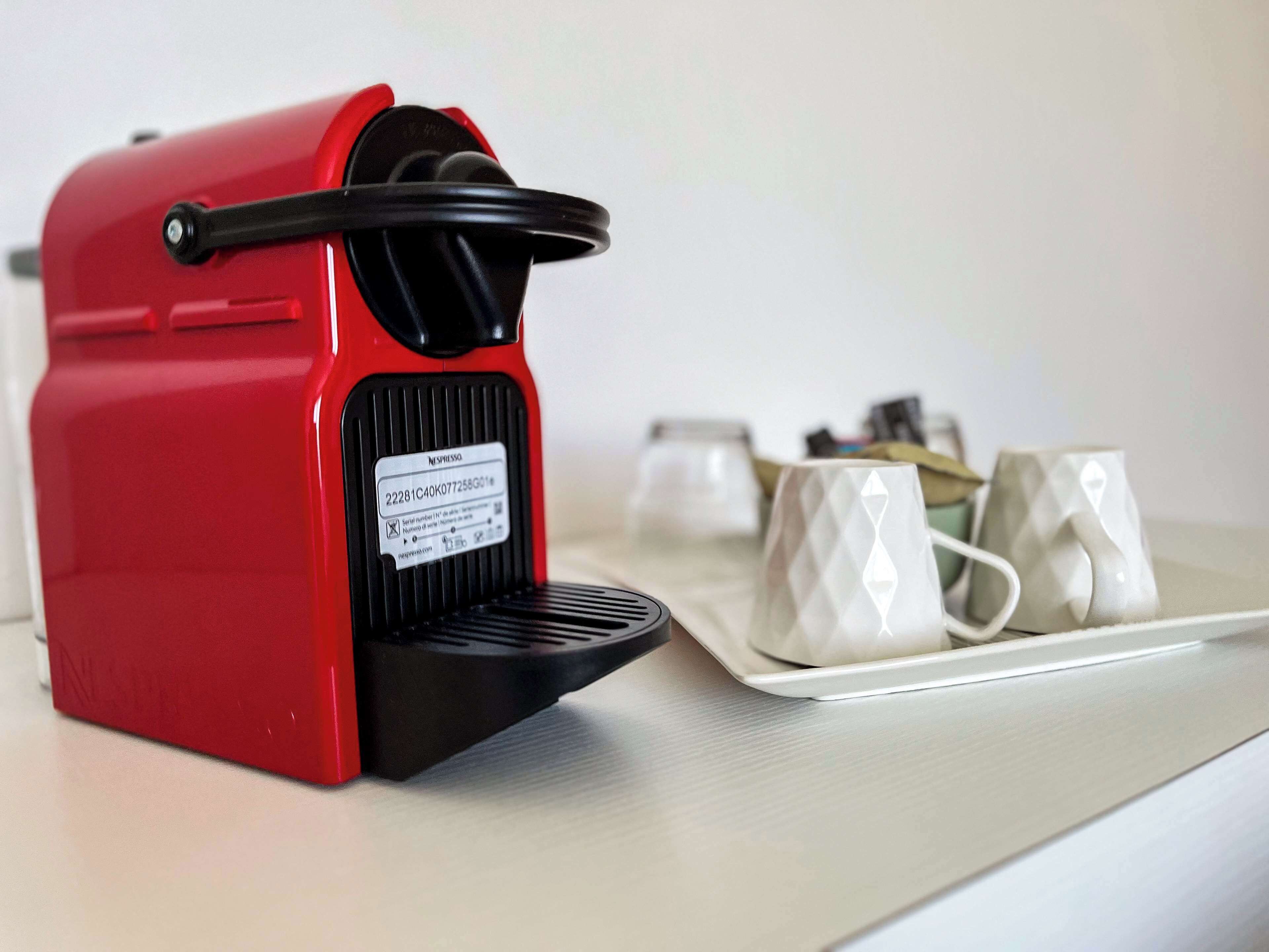 A red Nespresso coffee machine with a tray of white cups.