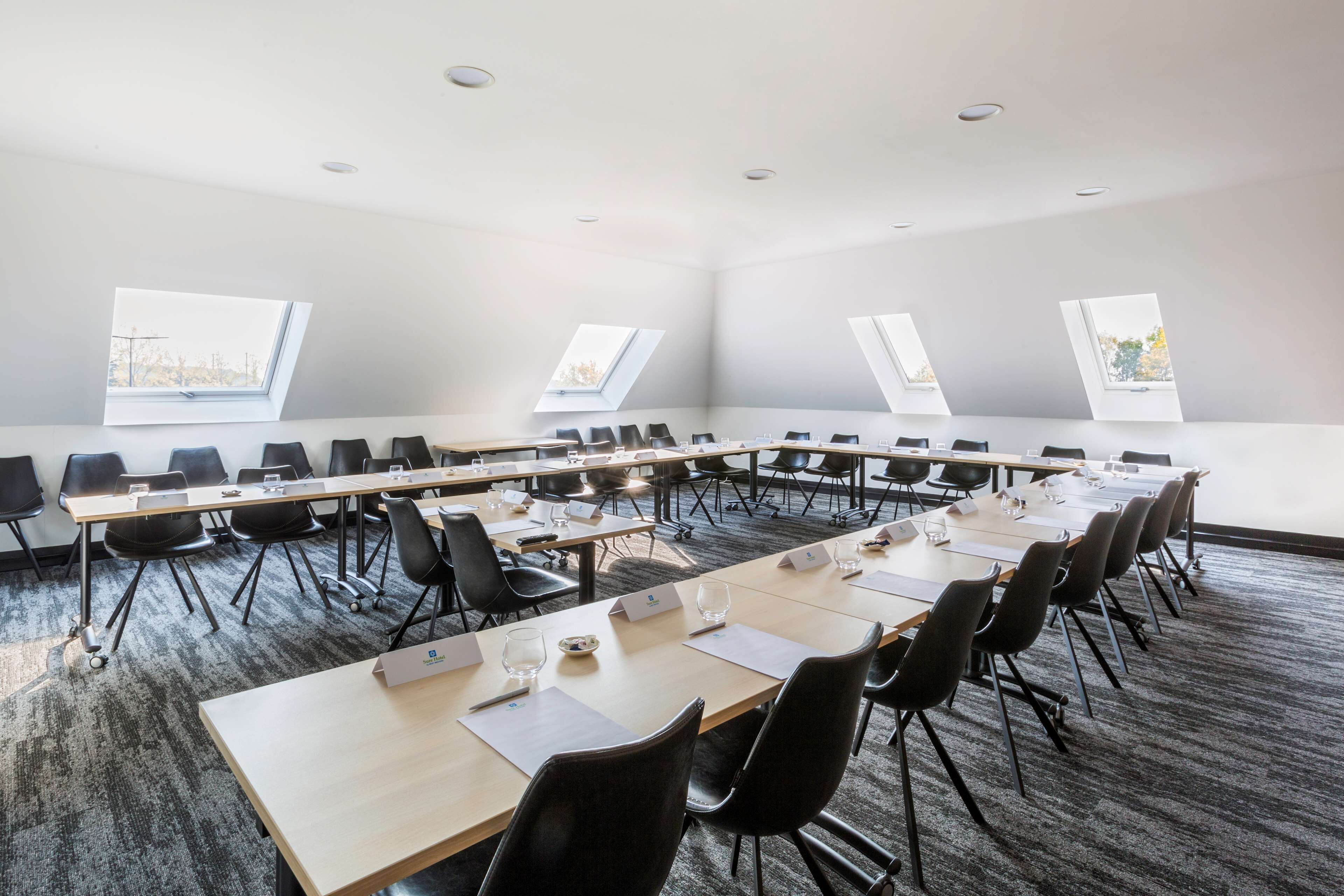 Ein Konferenzraum mit langen Tischen, schwarzen Stühlen und Dachfenstern.