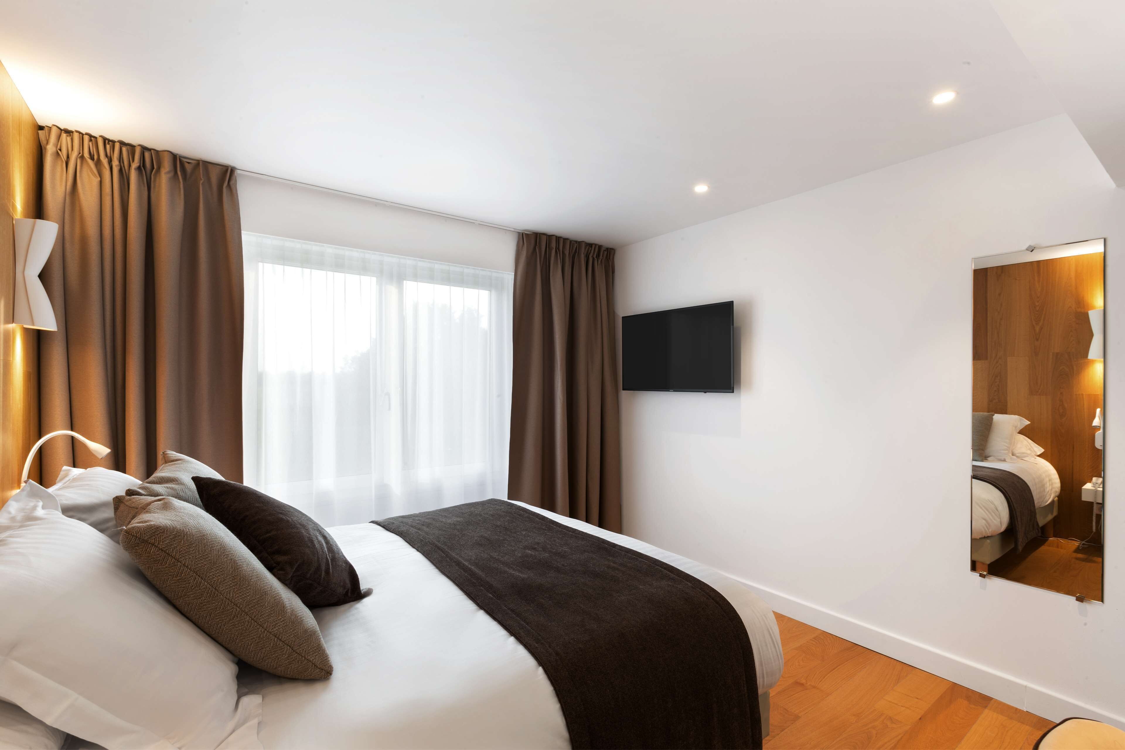 A modern hotel room with a large bed, a flat-screen TV, and a mirror on the wall.