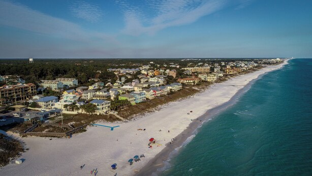 Un pueblo costero con una extensa playa de arena, propiedades frente al mar y un faro a lo lejos.