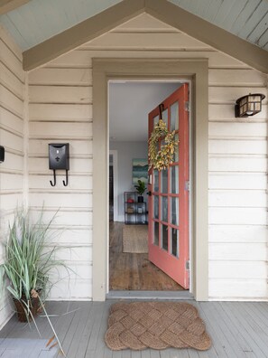 Entrada de una casa de madera con una puerta roja, un buzón y una planta en maceta.