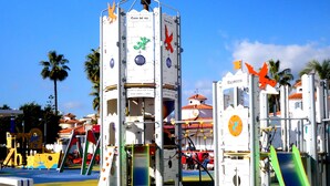 A playground with climbing structures and slides, surrounded by palm trees and buildings. - Newly renovated dream apartment with all amenities (Torrox Costa)