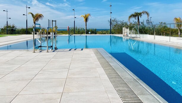 A clear blue swimming pool with a tiled deck, surrounded by palm trees and street lamps, under a clear sky. - Newly renovated dream apartment with all amenities (Torrox Costa)