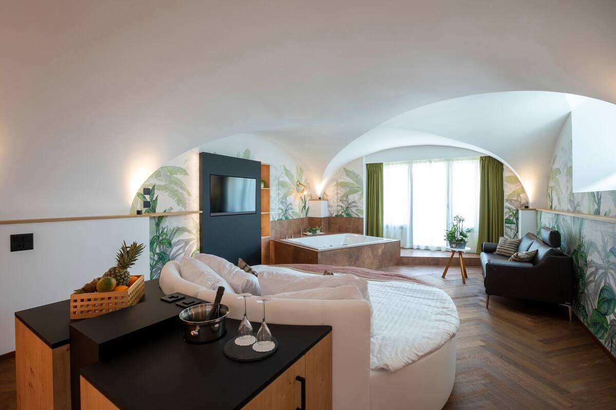Een moderne, goed verlichte kamer met een rond bed, een klein ziteplaats voor een maaltijd en een zithoek met een bank en een tafel.