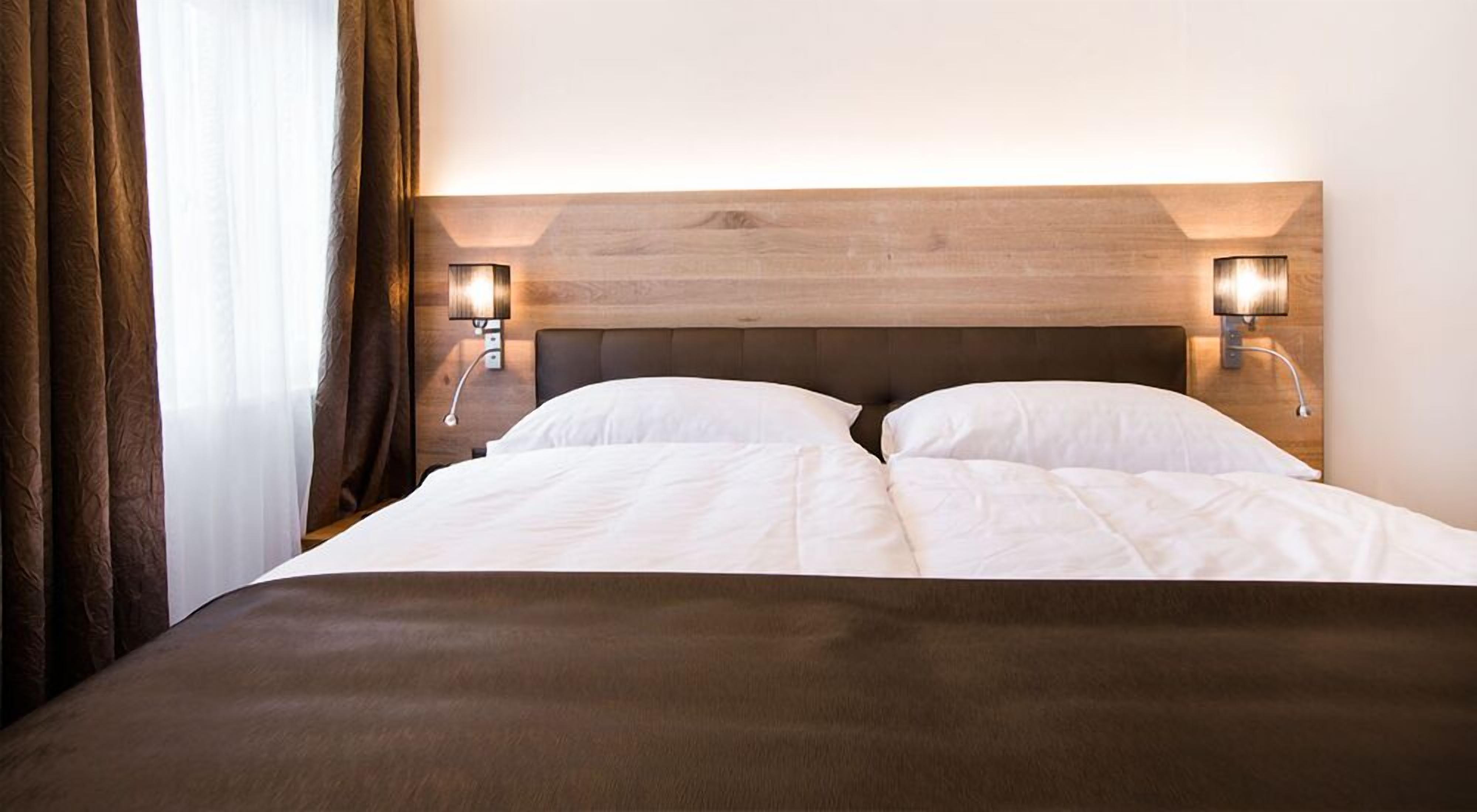 Una habitación de hotel con una cama grande, dos lámparas de noche y un cabecero de madera.