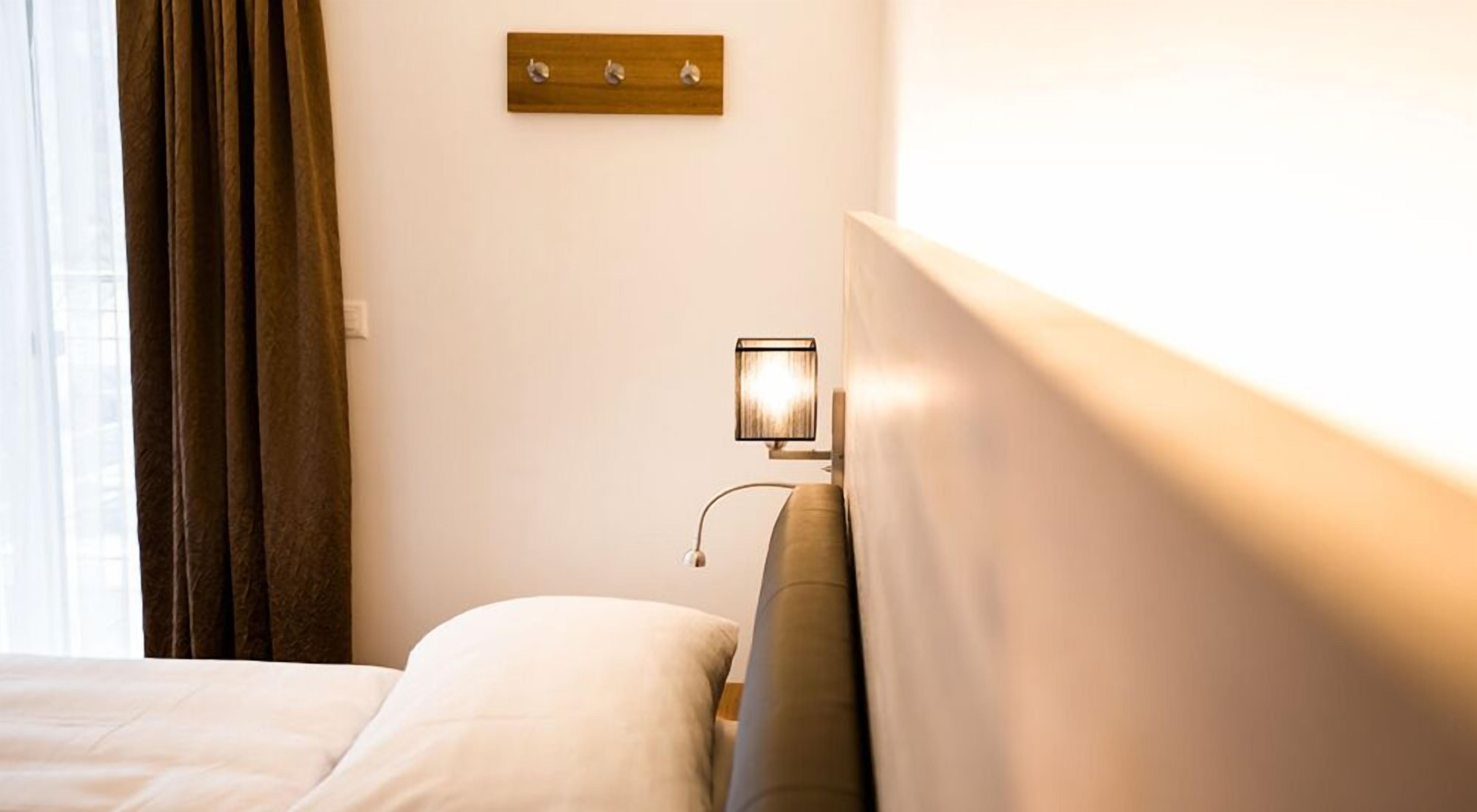Habitación de hotel con una cama, una mesita de noche con una lámpara y un panel de madera encima de la mesita.
