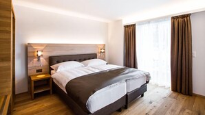 Een moderne hotelkamer met een groot bed, houten vloeren en uitzicht op de stad door grote ramen.