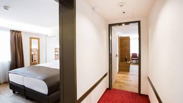 A hotel room with a bed, a mirror, a door leading to a hallway, and a red carpet.