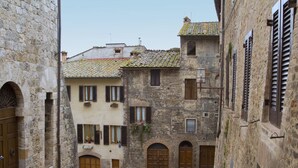 A narrow street flanked by historic stone buildings with arched doorways and wooden shutters.