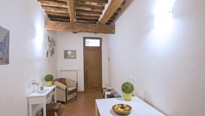 A small, cozy room with a wooden ceiling, a white table with a bowl of fruit, a red chair, and a small table with a plant.