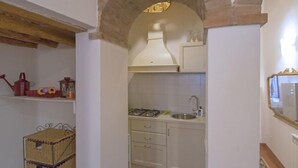 A compact kitchen with a gas stove, sink, and white cabinets. There is a wooden shelf with decorative items and a wicker basket.