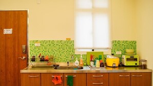 A compact kitchen with a wooden door, green tiled backsplash, and a window above the sink. - Happy Tree Hostel (Jinning)