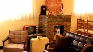 A living room with a brick fireplace, a wooden coffee table, a leather sofa, and a vintage television. - Happy Tree Hostel (Jinning)