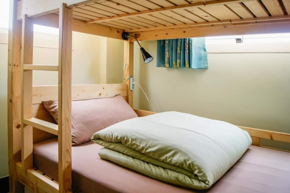 Una cama litera con estructura de madera, una cama individual en la parte inferior y una lámpara en la pared.