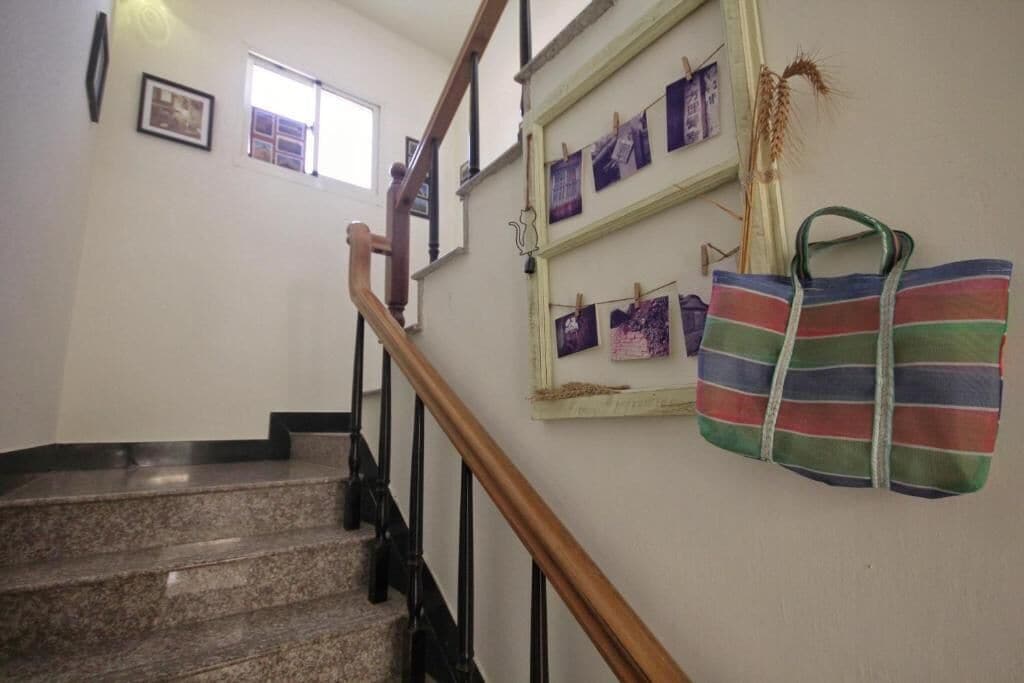 A staircase with a wooden handrail and a wall with framed pictures and a striped bag.