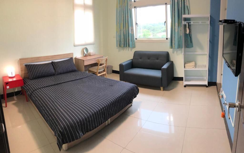 A bedroom with a bed, a desk, a chair, a sofa, and a TV.